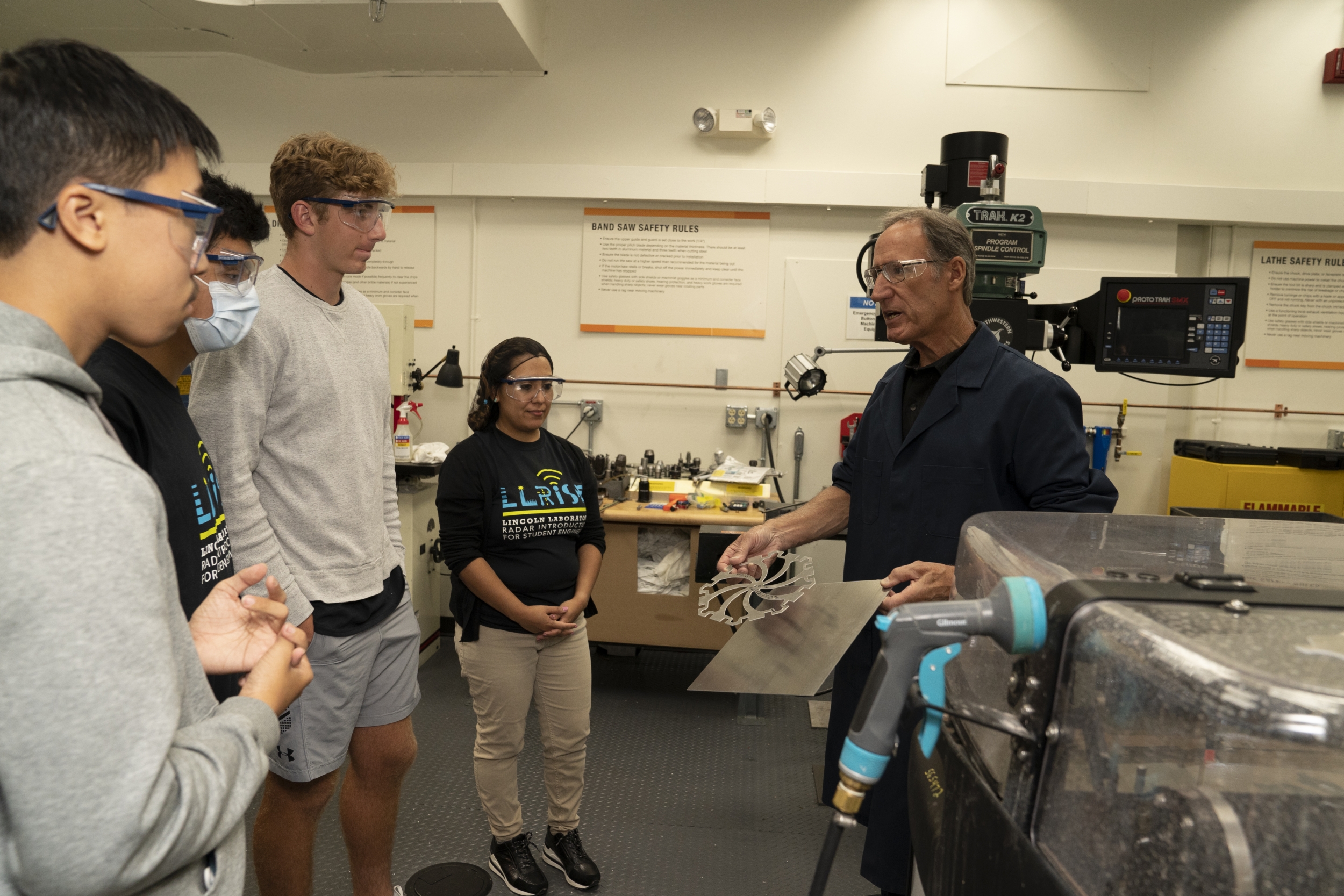 A photo of teachers and students in a lab with a waterjet laser cutting machine and a steel piece it produced.