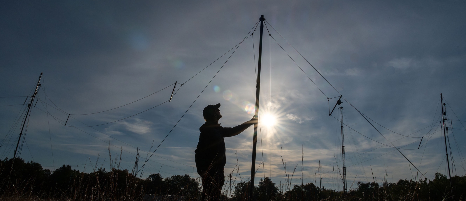 A man inspects an antenna at sunrise.