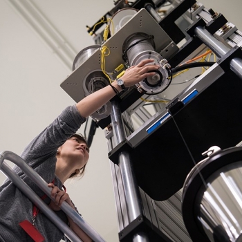 A researcher adjusts the fiber draw tower as it pulls and spools a fiber.