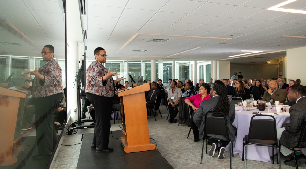 Robbin Chapman stands at a podium and addresses attendees seated at the luncheon. 