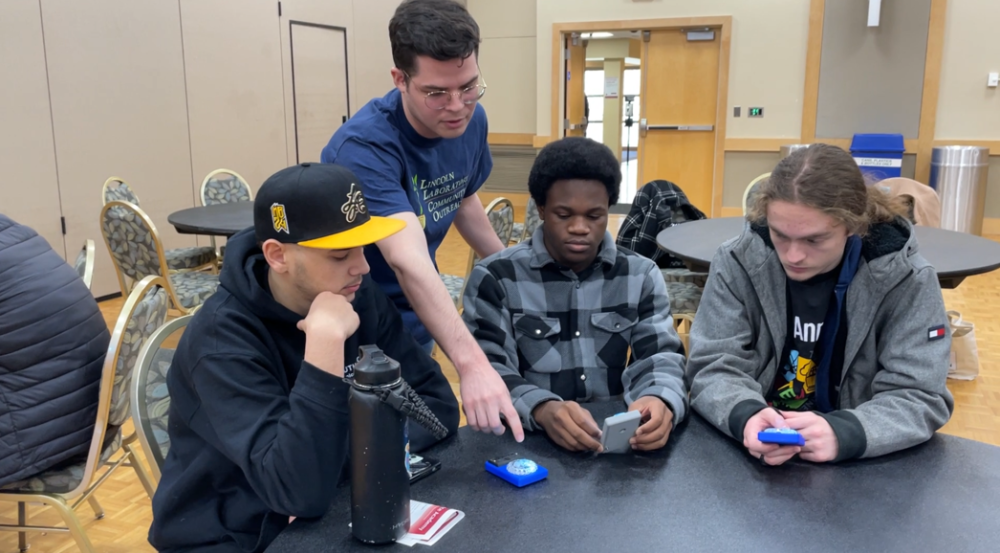 David Langus Rodriguez of Lincoln Laboratory helps three students use development boards.