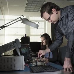 A photo of two staff members with electronic equipment in front of them in a lab