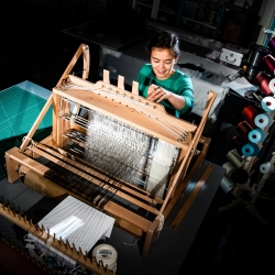 A women stands in front of a fabric weaver 