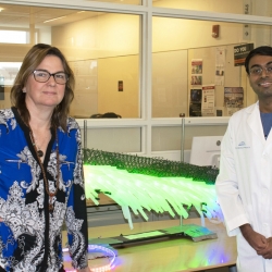 Two scientists stand in a laboratory in front of a green-lit sculpture 