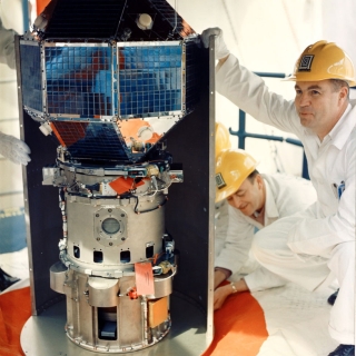 Engineers inspect LES-1 prior to its 1965 launch. The satellite is positioned atop a Titan III rocket on the launch pad at Cape Kennedy, Florida.