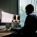 A man sits at an office desk looking at a large monitor. the left hand side shows data graphs, the right side shows two images of the back of a woman's arm with a crown tattoo, and a green box around the tattoo. 